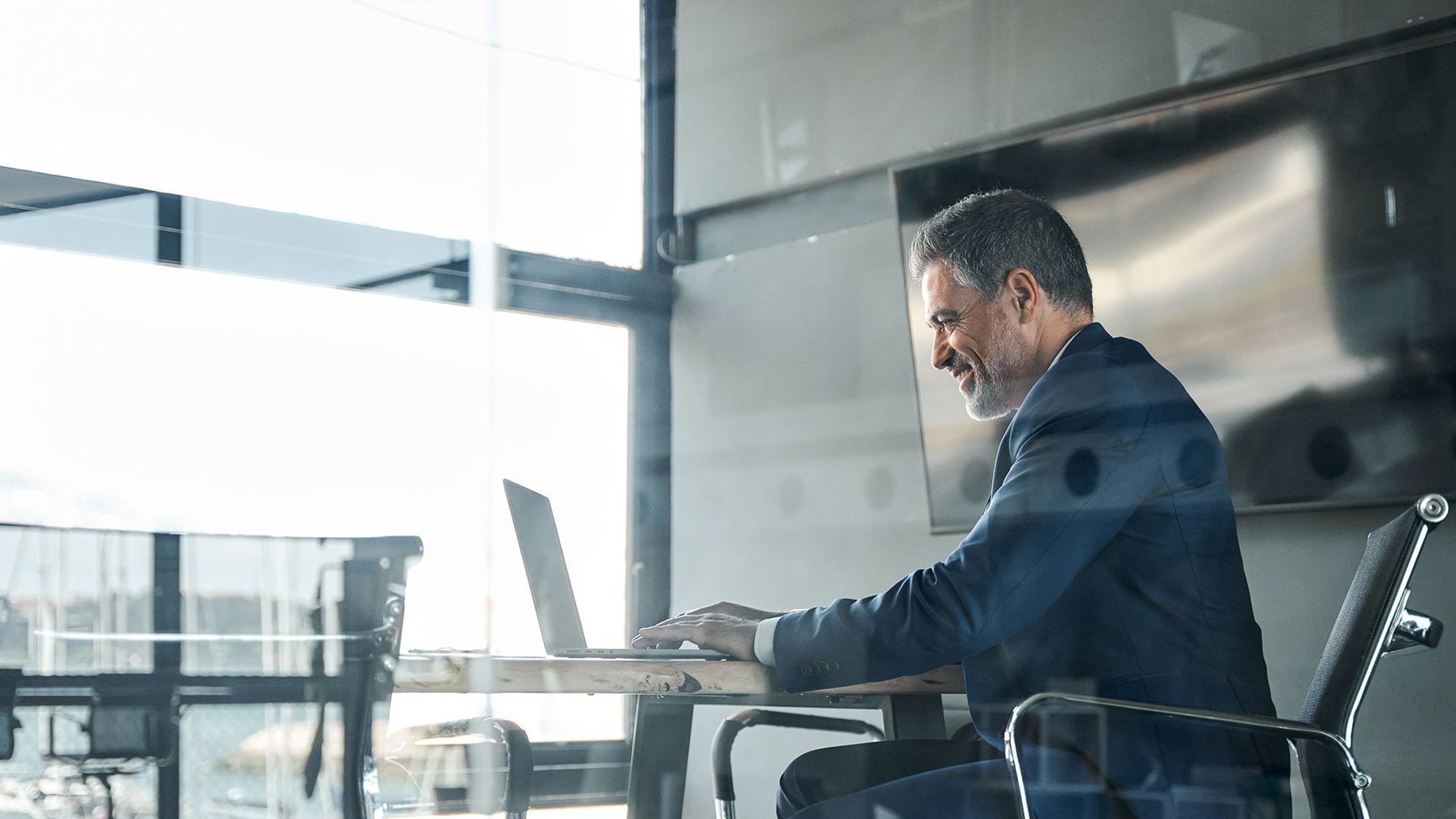 Professional businessman in a suit working on a laptop in a bright, modern office. 