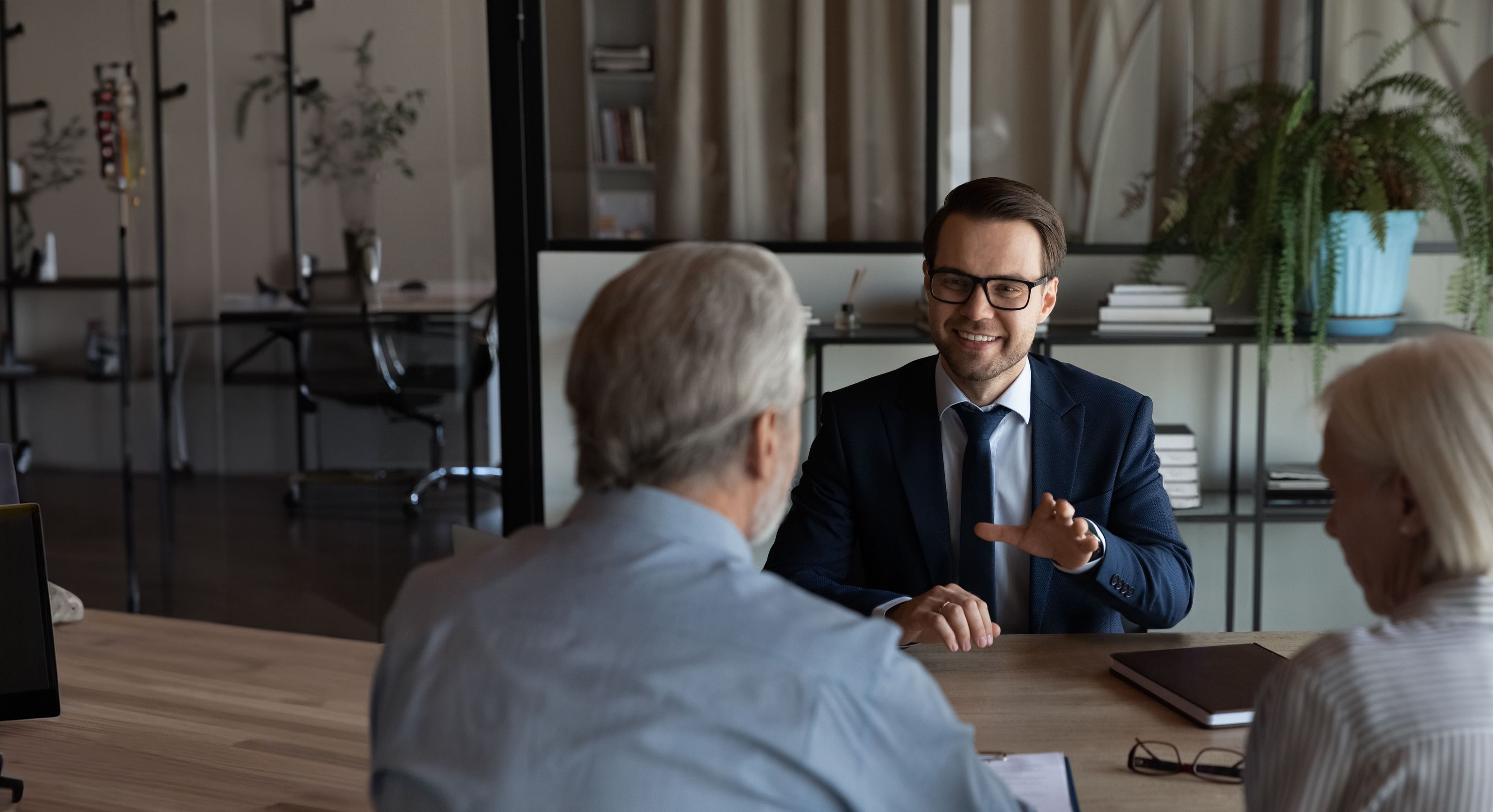 A professional financial advisor in a suit discussing investment strategies with senior clients in a modern office.