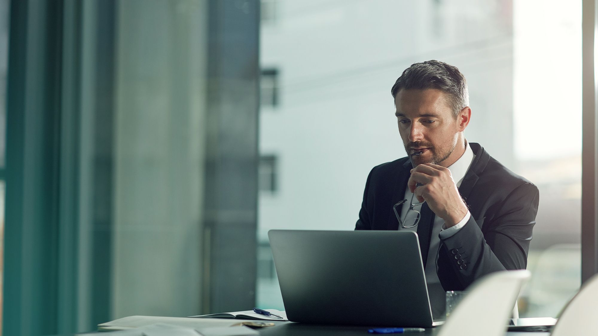 Professional businessman in a suit working on a laptop in a bright, modern office.