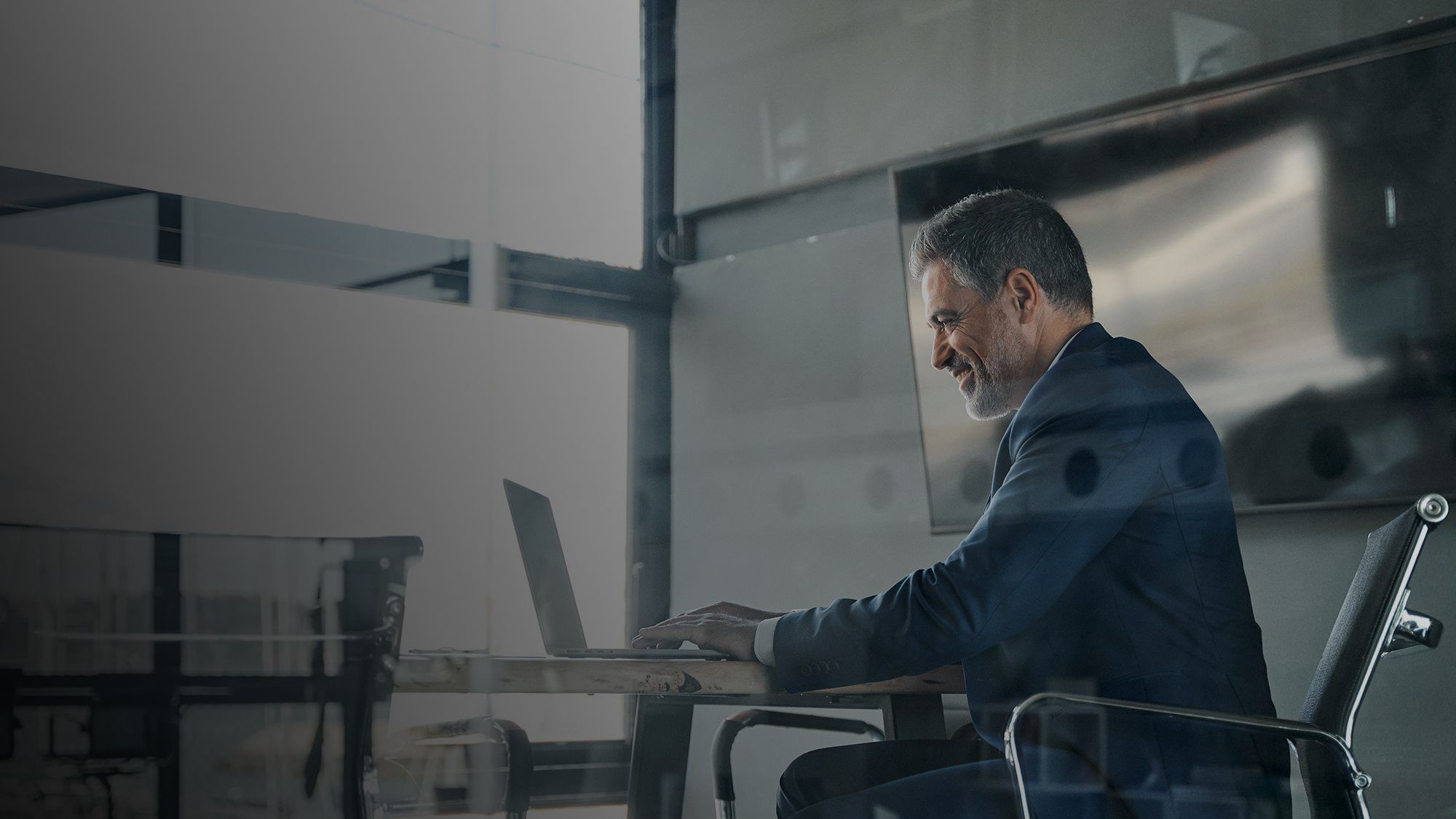 Professional businessman in a suit working on a laptop in a bright, modern office.