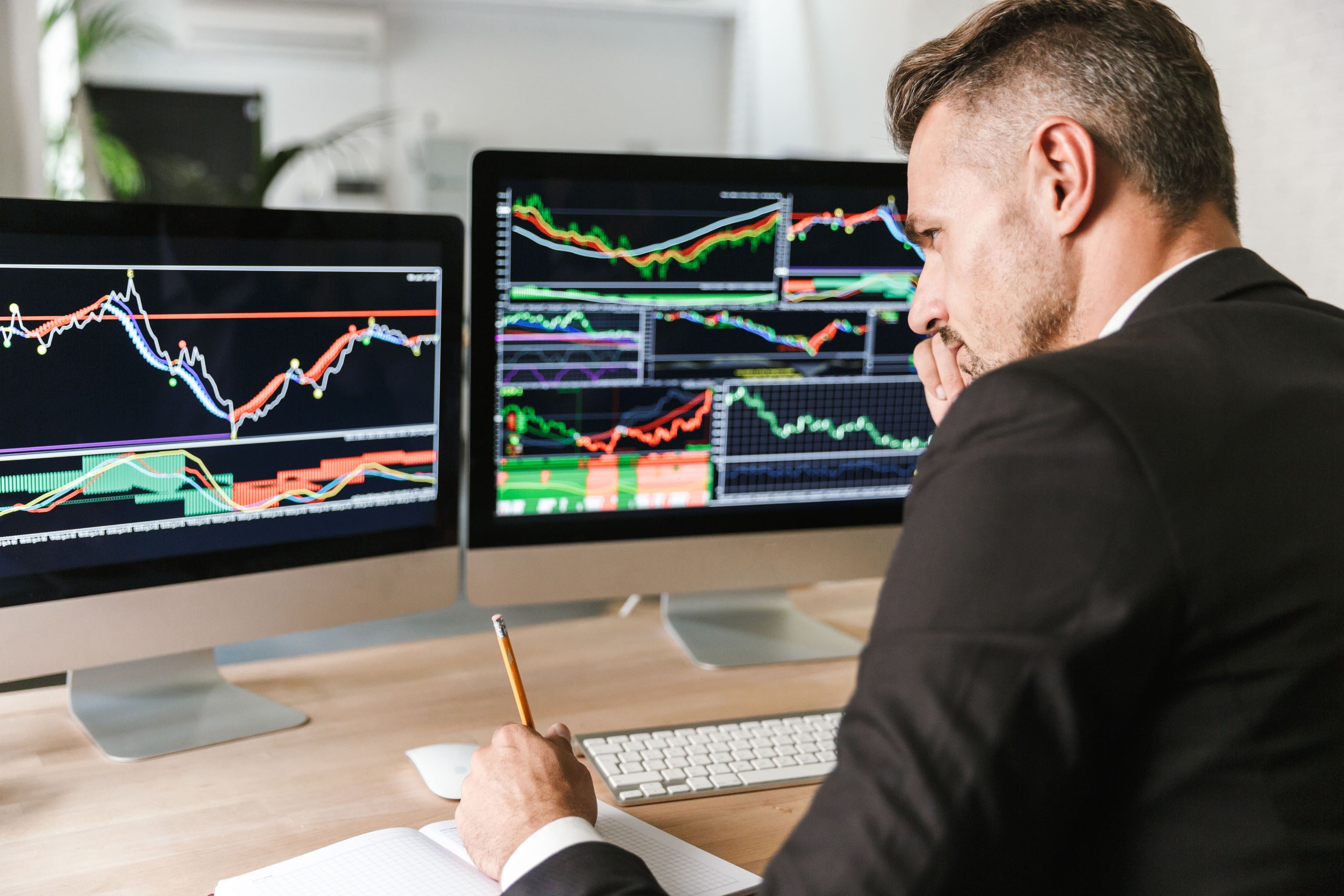 A professional investor analyzing stock market trends on multiple screens in a modern office. 