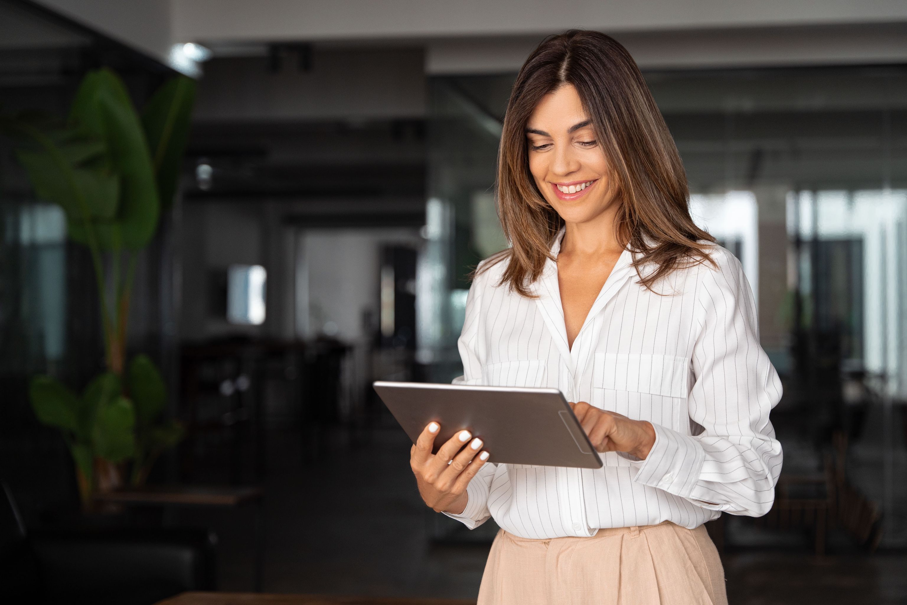 A confident businesswoman in a stylish white blouse working on a tablet in a contemporary office.