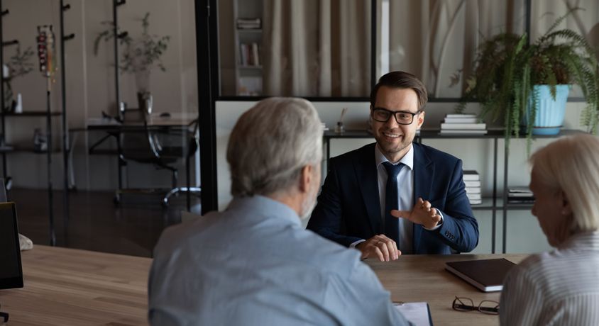A professional financial advisor in a suit discussing investment strategies with senior clients in a modern office.