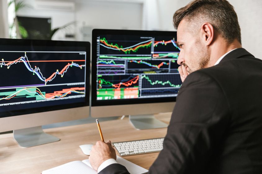 A professional investor analyzing stock market trends on multiple screens in a modern office. 
