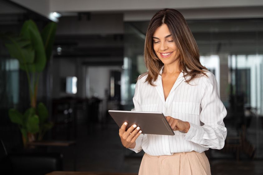 A confident businesswoman in a stylish white blouse working on a tablet in a contemporary office.
